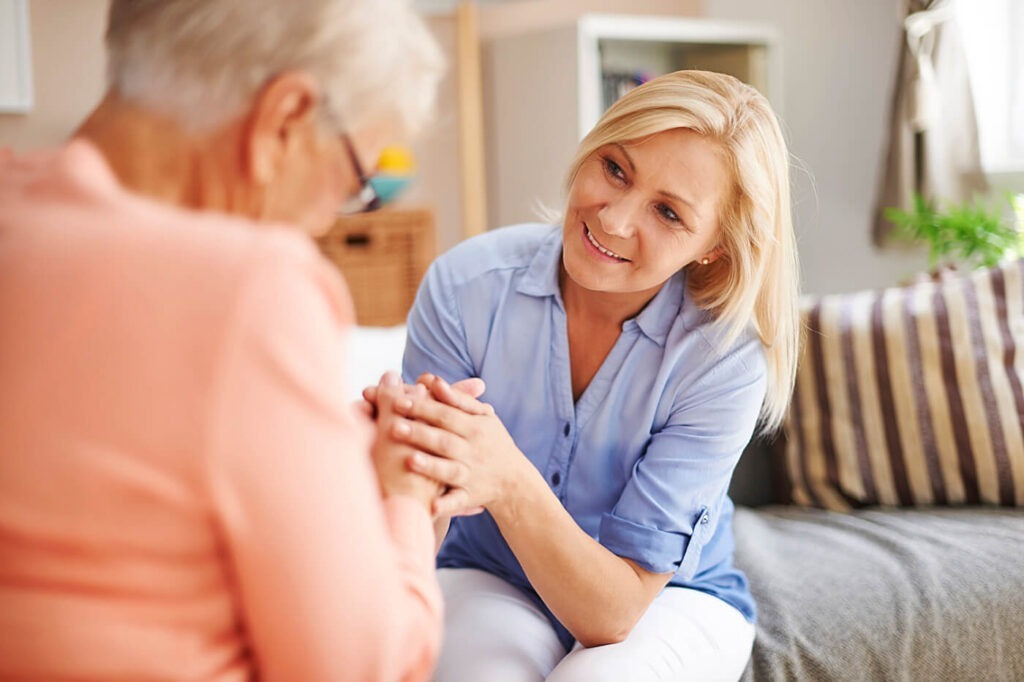 Eine Tochter hält tröstend die Hand ihrer pflegebedürftigen Mutter.