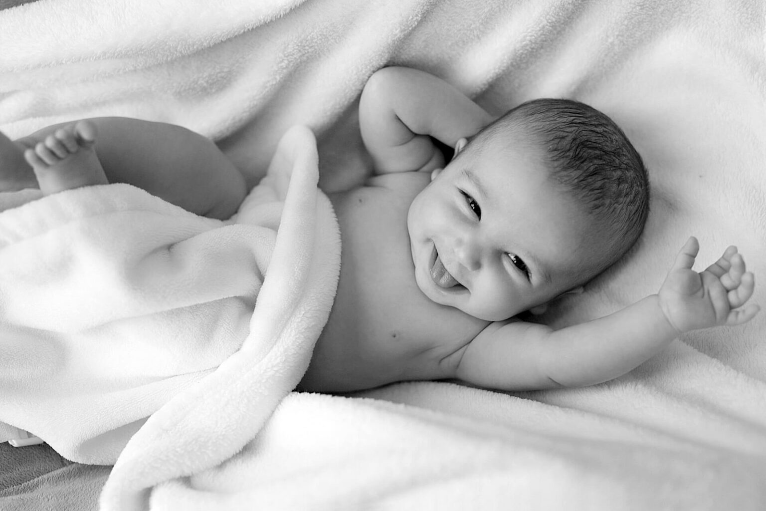 Ein Baby, das in einem Bettchen liegt, lächelt uns an.