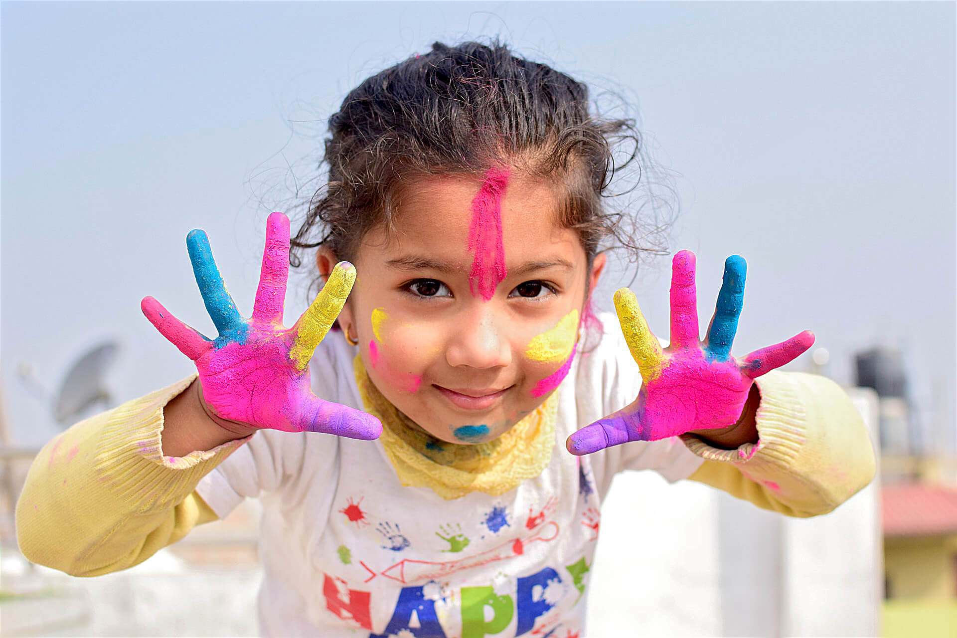 Ein fröhliches Mädchen bei einem Holi-Fest, Gesicht und Hände mit farbigem Pulver bemalt