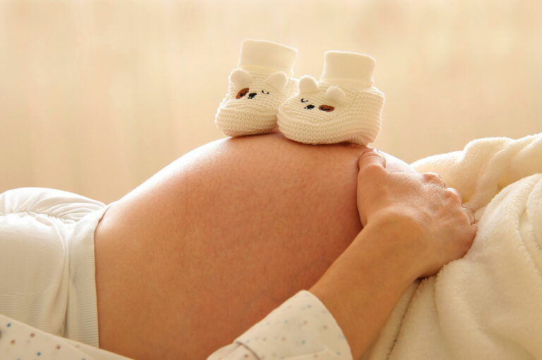 Babyschuhe auf dem Bauch einer hochschwangeren Frau
